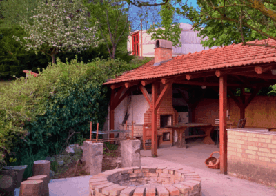 Az Ezerdomb Pihenőház tágas Szaletlije és a tűzrakóhely, zöld környezetben, nyári fényekkel.